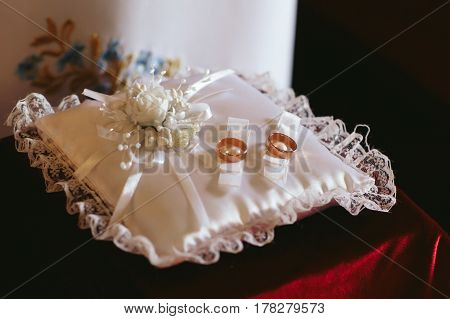 Golden wedding rings lie on the white silk pillow