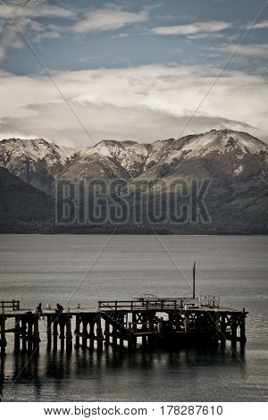 Two people on a dock, in a Patagonian Lake, with mountains sourrounding them