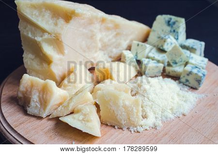 Grated Parmesan and sliced Blue cheese with chili pepper on wooden chopping board on dark background. Tasty appetizers. Selective focus.