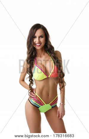 Gorgeous long haired brunette with perfect body posing with a tender smile dressed in fine colorful bicini in studio