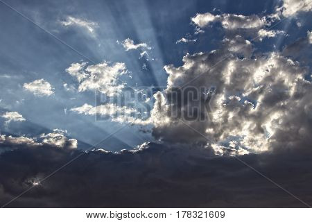 Inspirational: Soft focus storm clouds with strong light rays, suitable for a background layer. Consists of dark storm clouds against a blue sky with light rays peaking through the clouds.