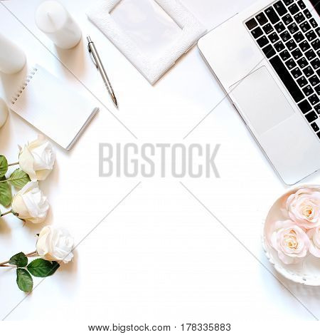 Minimalistic feminine workplace with laptop keyboard, pen, white candles, notebook and roses in flat lay style. White background, top view, frame