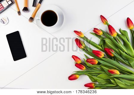 Creative background with make up brushes, mobile phone, cup of coffee and flowers on white background. Top view. Flat lay