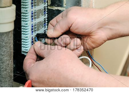 Man's hands inserts wires in a switch for thermostats and servo drives valves in a home heating system.