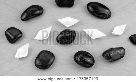 White paper boats in sigle file between abstract rock stones. Black and White. Shot from Top Perspective.