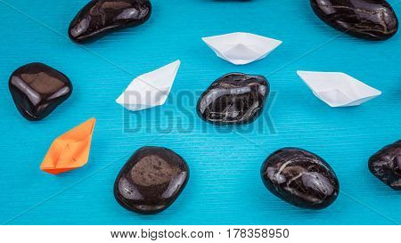 Red paper Leadership lead shite ships in sigle file between abstract rock stones on blue background.