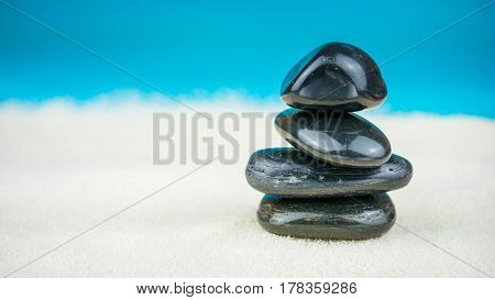 Growing piled up of black pebbles on bright sand with blue background.