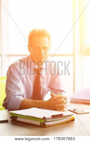 Toned of kind businessman sitting in office and waiting for his colleagues to have meeting. Handsome man happy smiling for camera while sun is shining.