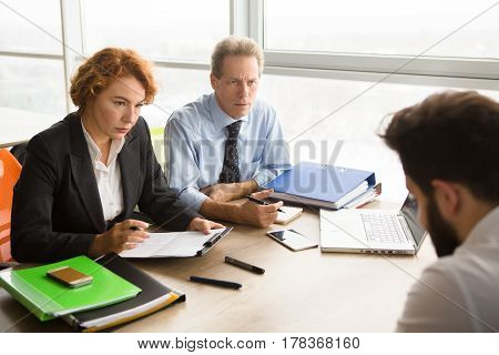 Business representatives man and woman communicating with new worker. Business people taking interview while sitting at table in office.