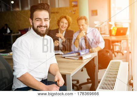 Happy entrepreneur man smiling after successful deal with huge company, firm, enterprise. His business colleagues sitting on background in office.