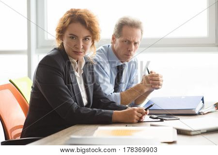 Business concept. Angry boss woman looking at camera while sitting in board room with her colleagues or workers in office. People negotiating.