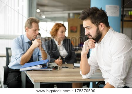 Young student looking sad, because he failed interview in office. Bearded man thinking how to get successful or positive assessment.