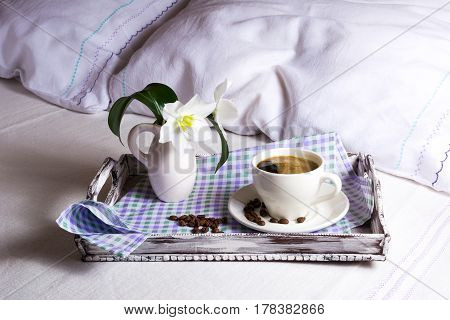 Cup of fresh coffee with white lily flowers in vase on rustic wooden serving tray. Tender love concept.