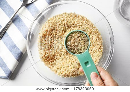 Measure scoop full of brown rice taken from glass bowl