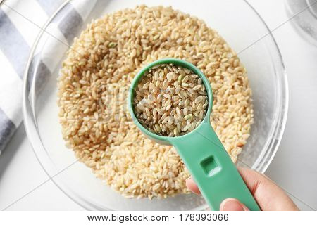 Measure scoop full of brown rice taken from glass bowl