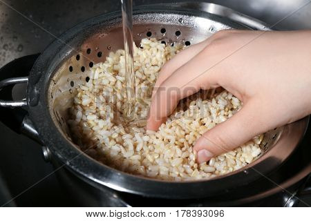 Female hand washing brown rice with water in colander