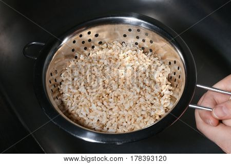 Female hand holding colander with brown rice