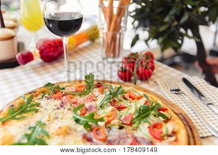 Pizza with cheese, tomato and meat, with glass of wine on served table with plaid tablecloth