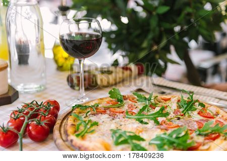 Pizza with cheese, tomato and meat, with glass of wine on served table with plaid tablecloth