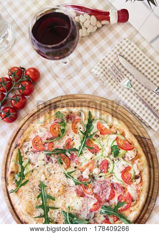 Pizza with cheese, tomato and meat, with glass of wine on served table with plaid tablecloth