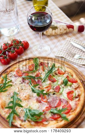 Pizza with cheese, tomato and meat, with glass of wine on served table with plaid tablecloth