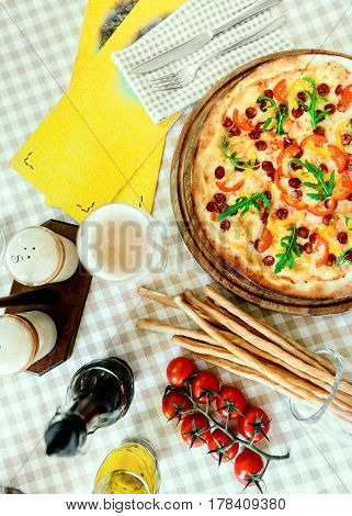 Tasty pizza with cheese, tomato and meat, with glass of beer on served table with plaid tablecloth
