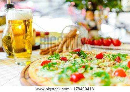 Tasty pizza with cheese, tomato and meat, with glass of beer on served table with plaid tablecloth