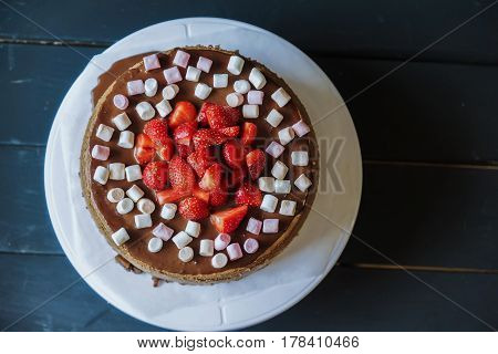 Delicious cake with fresh strawberries and dark chocolate sauce and plate with marshmallows, top view