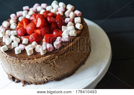 Delicious cake with fresh strawberries and dark chocolate sauce and plate with marshmallows
