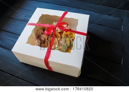 Cake with meringue and orange decoration in box with transpatent top and ribbon with bow