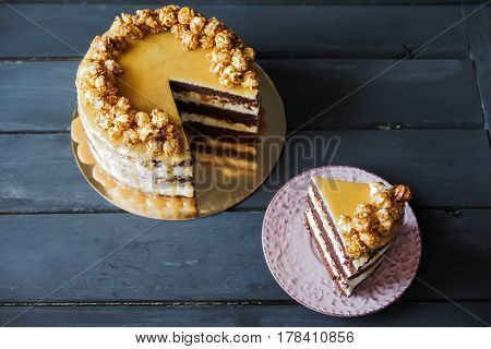Delicious cake with caramel popcorn and caramel sauce and plate with slace of this cake