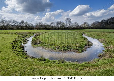 small stream winds its way through the green meadow and makes a sharp turn