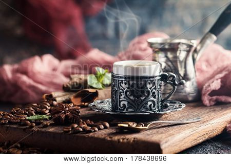 Turkish coffee in traditional embossed metal cup with coffee beans on black backfround. Toned photo
