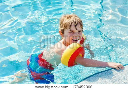 happy little kid boy having fun in an swimming pool. active happy child learning to swim. with safe floaties or swimmies. family, vacations, summer concept.