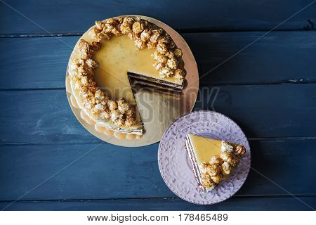 Delicious cake with caramel popcorn and caramel sauce and plate with slace of this cake, top view