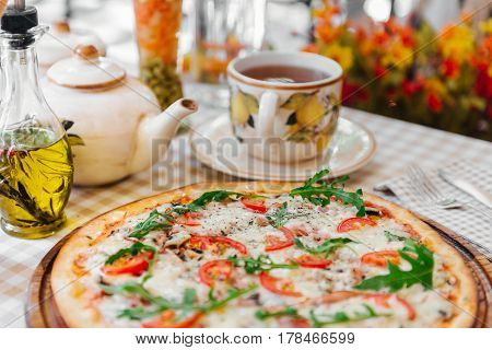 Pizza with cheese, tomato and meat, with cup of tee on served table with plaid tablecloth