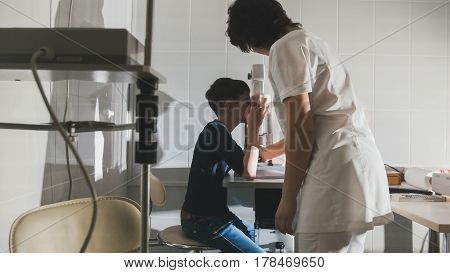 Woman optometrist examining pre adolescent boy's eyes in ophthalmology clinic, hotizontal