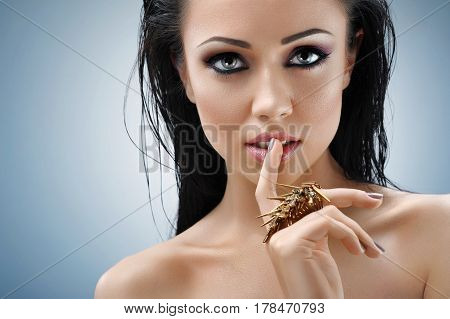 Sensual posing. Studio close up portrait of a gorgeous dark haired woman wearing dark eye makeup looking to the camera pressing her finger to her lips copyspace gesture quiet silence seduction sexy