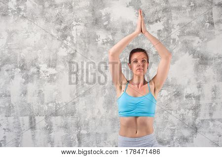 Beautiful caucasian woman doing yoga against grey wall. Fit girl wearing sportswear exercising indoors.