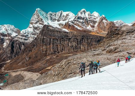 Group of Athletes of different Age and Ethnicity young and mature Caucasian and Asian moving across Glacier in high Altitude Mountains with Summits and Walls View on Background.