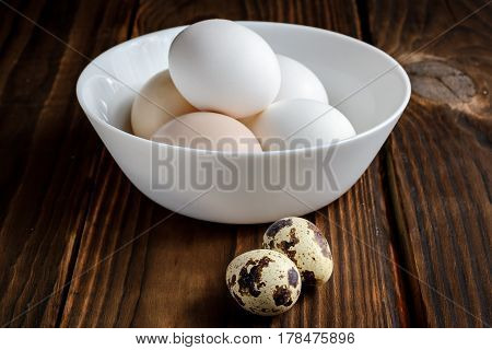 Chicken eggs in a plate and quail eggs on a wooden background closeup