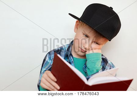 A photo of young schoolboy hard at work sitting with his hand on his cheek reading a book leraning new material preparing for the lessons. Young boy having tired expression while reading