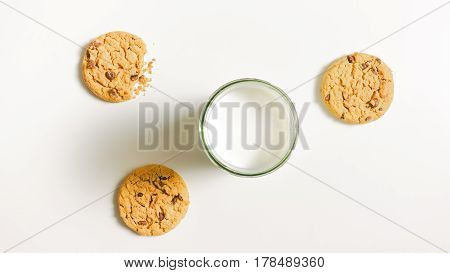 Three round friable cookies and a full glass of milk on the table. One cookies is bitten