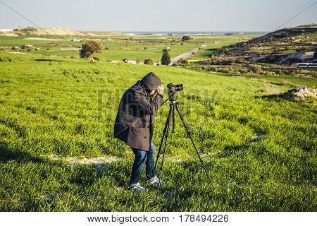 A photographer or traveller using a professional DSLR camera on a tripod in the nature for background