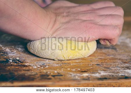 Ball of dough knead with hands on a rustic wooden table with dusting flour. Close up.