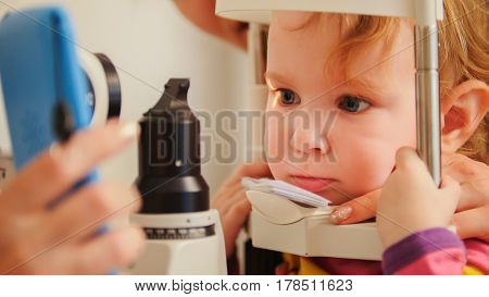 Child's optometry - little girl checks eyesight in eye ophthalmological clinic - close up, telephoto