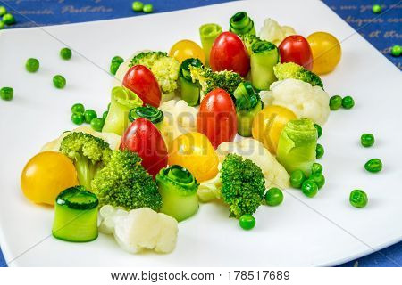 Vegetables tomatoes cucumbers peas and broccoli on a white plate