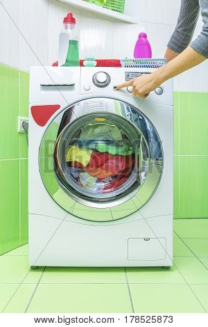 A woman's hand presses a button on the washing machine. Start the wash cycle.