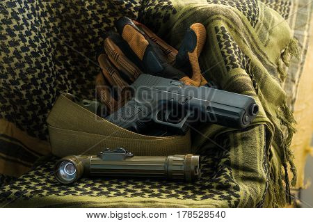 Composition of gun angle-head flashlight tactical gloves and strap belt lying on shemagh