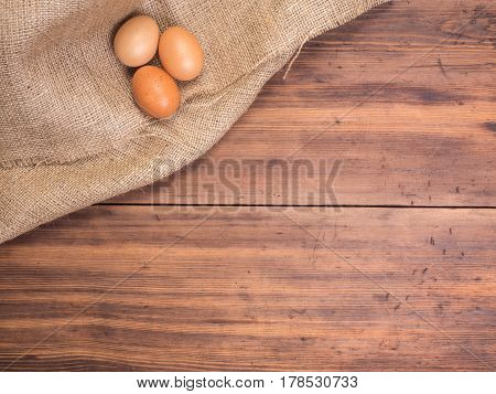 Chicken eggs on old rural wooden table boards and burlap vintage background, photo top view. Hessian, sacking texture with eggs on wooden background for design, Easter greetings card or advertisement